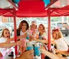 A group of joyful friends are toasting with drinks while enjoying a ride on a pedal pub