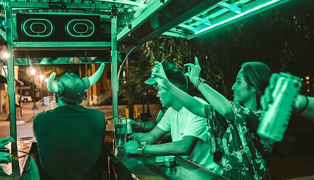 A group of people are enjoying a night out with one person wearing a viking helmet at what appears to be an outdoor bar or food stand highlighted by neon lighting