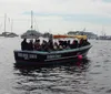 A group of people are enjoying a boat tour at dusk with a city skyline in the background