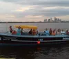 A group of people are enjoying a boat tour at dusk with a city skyline in the background