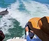 Two people are watching a dolphin leap out of the water behind their boat