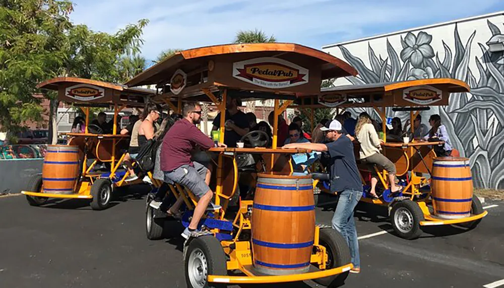 A group of people enjoys pedaling together on a mobile bar on wheels known as a pedal pub decorated with faux barrels