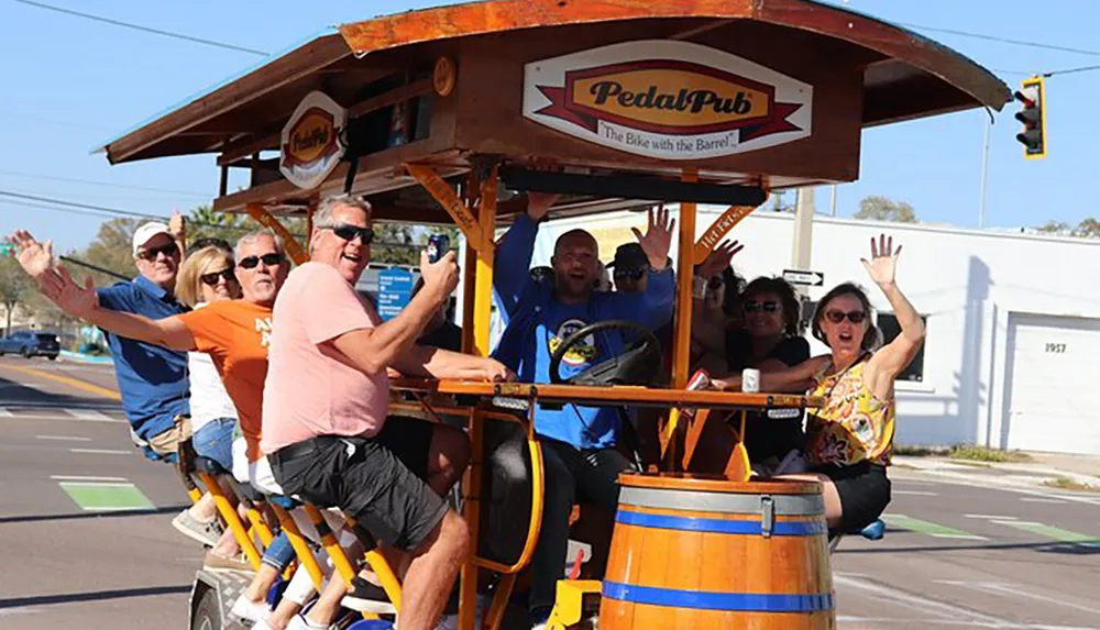 A group of people is joyfully riding a pedal-powered bar on wheels down a street