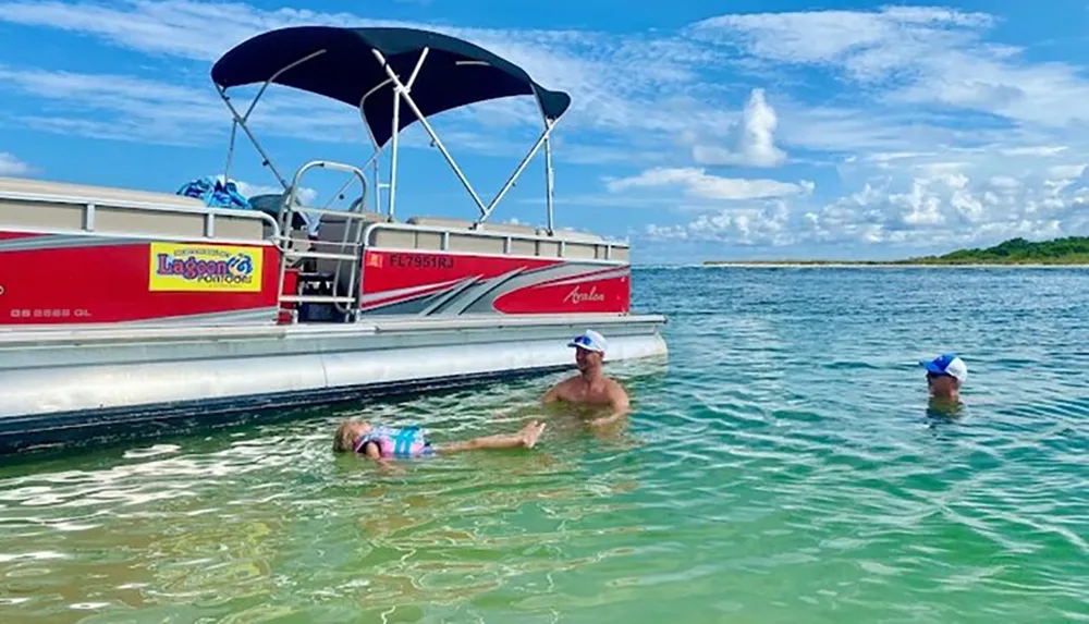 The image shows people enjoying a day in the water near a red and silver pontoon boat under a blue sky dotted with clouds