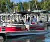 A group of people is enjoying a sunny day on a red pontoon boat at a marina filled with various boats and yachts