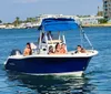 A group of people enjoy a sunny day on a blue motorboat on calm waters with coastal buildings in the background