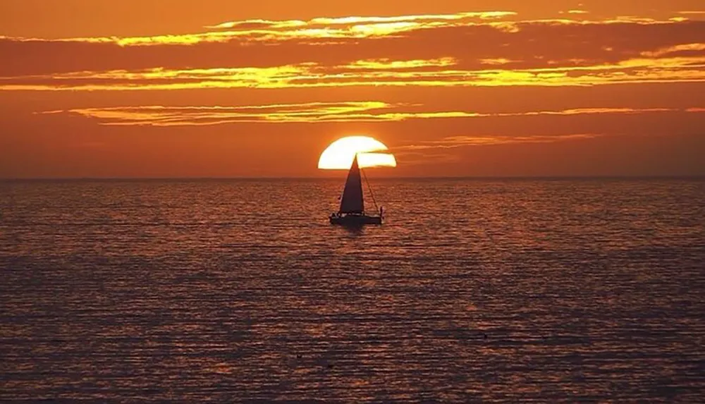 A sailboat is silhouetted against a stunning sunset over the ocean