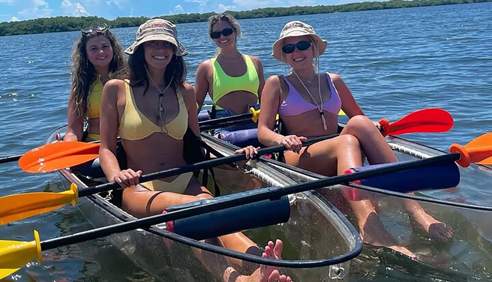 Four individuals are happily kayaking together on a sunny day donning swimwear and hats with paddles in their hands