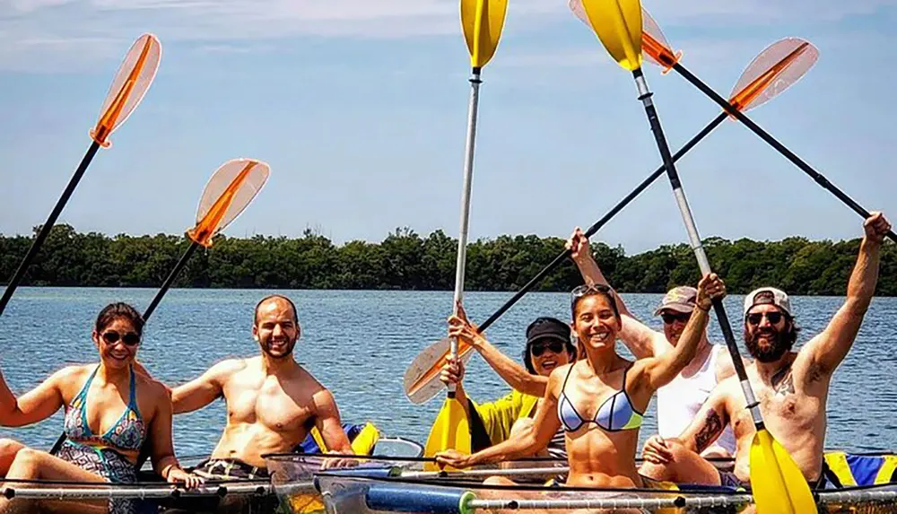 A group of happy people are kayaking together raising their paddles in celebration on a sunny day