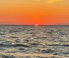 A person is posing with their hand outstretched as if holding the sun during a vibrant sunset by the sea