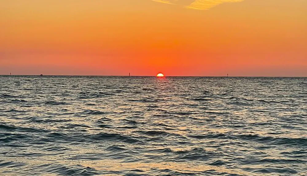 The image captures a serene sunset with the sun dipping into the ocean horizon under a gradient sky of orange and blue hues