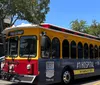 A colorful red and yellow trolley-style bus is parked on a city street adorned with advertisements and signage indicating it serves the Central Avenue route to St Pete Pier