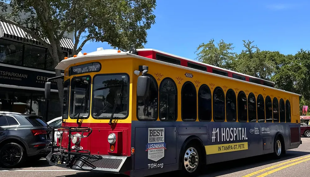 A colorful red and yellow trolley-style bus is parked on a city street adorned with advertisements and signage indicating it serves the Central Avenue route to St Pete Pier