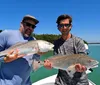 Two men are proudly displaying their catch of two large fish while standing on a boat with a clear blue sky and tranquil blue waters in the background