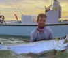 Two men are proudly displaying their catch of two large fish while standing on a boat with a clear blue sky and tranquil blue waters in the background