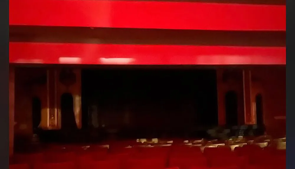 The image is a blurry view of an interior possibly a theater with red seats and a dark stage area