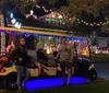 Two people are standing by a festively decorated golf cart in front of a house adorned with colorful Christmas lights at night