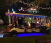 Two people are standing by a festively decorated golf cart in front of a house adorned with colorful Christmas lights at night