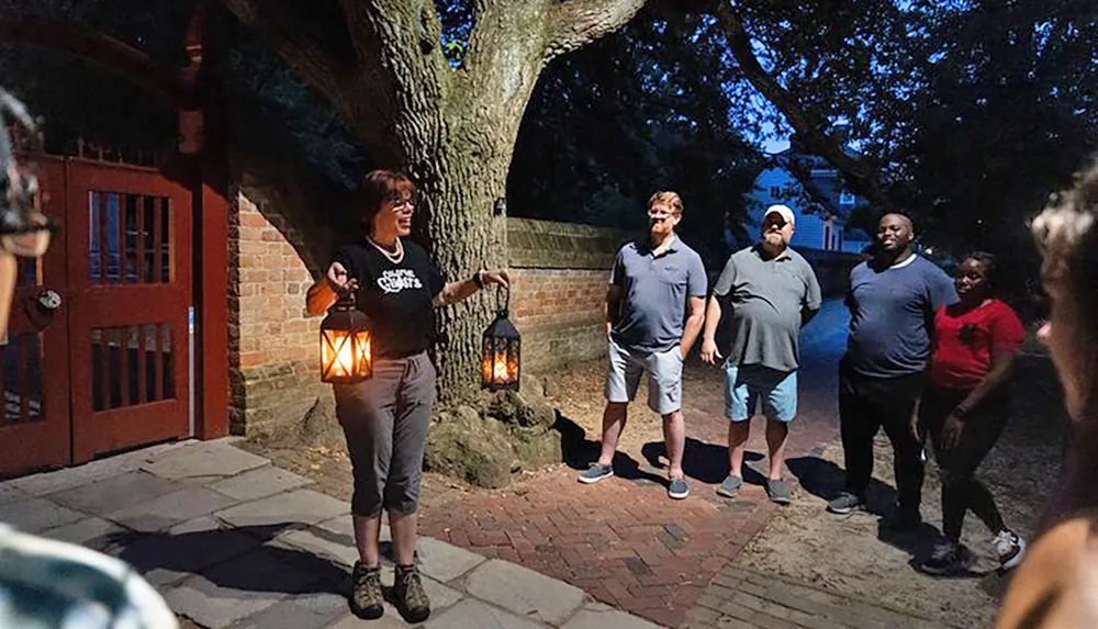 A guide holding lanterns is speaking to a group of people during an evening outdoor event