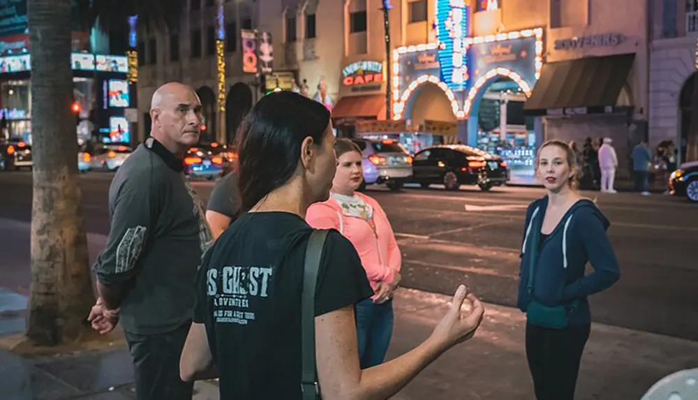 The image captures a nightly urban scene where four individuals seem to be engaged in a conversation on a busy street with bright neon signs and traffic in the background