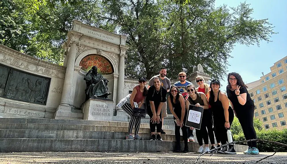 A group of people is posing for a photo in front of the Hahnemann Memorial in a sunny outdoor setting