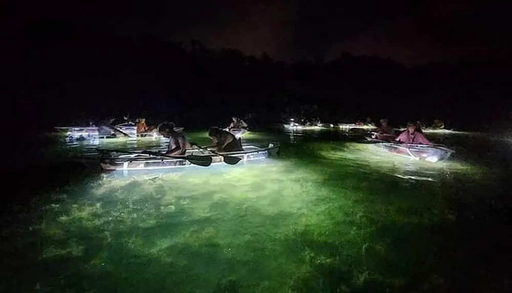 People are night kayaking with underwater lights illuminating the water around them