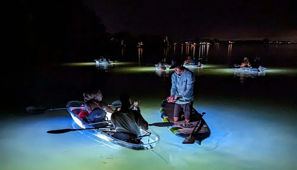 A group of people are night paddling on glowing kayaks illuminating the water beneath them