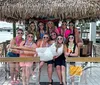 A group of smiling people wearing matching heart-shaped sunglasses is posing for a photo in a festive atmosphere by the waterfront with a city skyline in the background