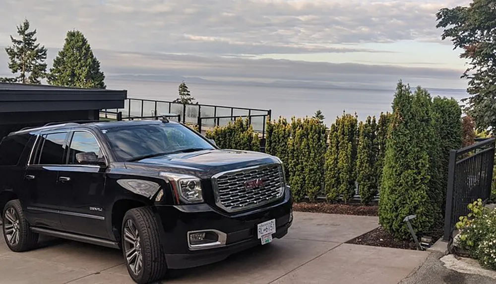 A black SUV is parked in a driveway with a scenic view of the ocean and horizon in the background