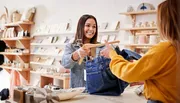 A smiling salesperson is handing a clothing item on a hanger to a customer in a boutique store.