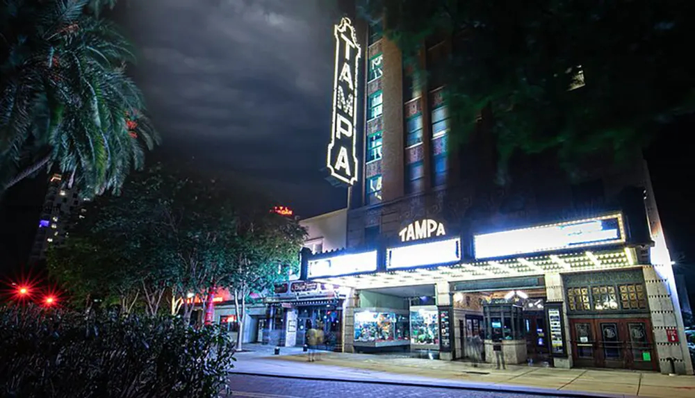 The image shows a neon-lit theater marquee at nighttime with the word TAMPA prominently displayed suggesting a historic or iconic venue in the city of Tampa