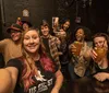 A group of cheerful people is taking a selfie in a bar raising their drinks to the camera