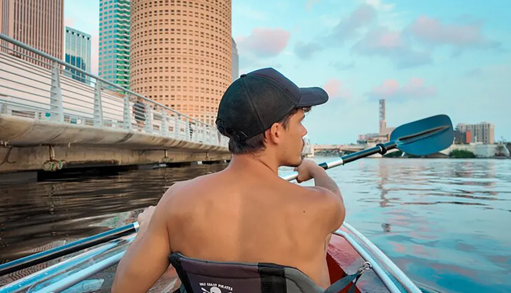 A person is kayaking in an urban river environment gazing at the cityscape ahead