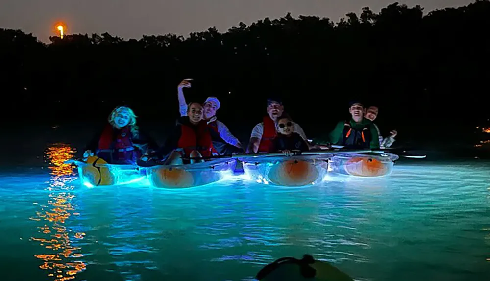 A group of people enjoying a night kayaking activity with illuminated kayaks on a body of water