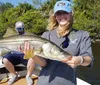 A smiling person is holding a caught fish on a sunny day with a fishing rod and reel in the background indicating a successful fishing trip