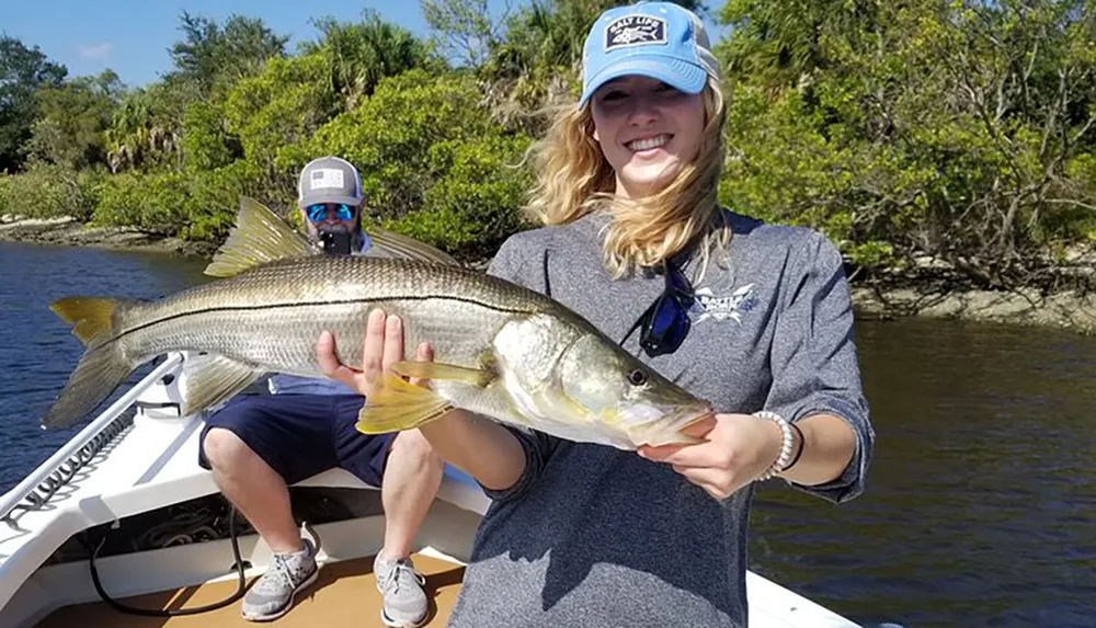 A smiling person is proudly holding a large fish on a boat with another person visible in the background