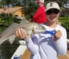 A smiling person is holding a caught fish on a sunny day with a fishing rod and reel in the background indicating a successful fishing trip