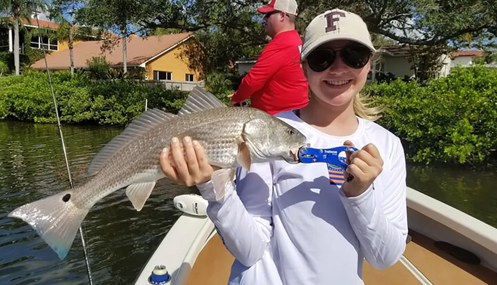 A smiling person is holding up a fish on a sunny day on a boat displaying a sense of accomplishment