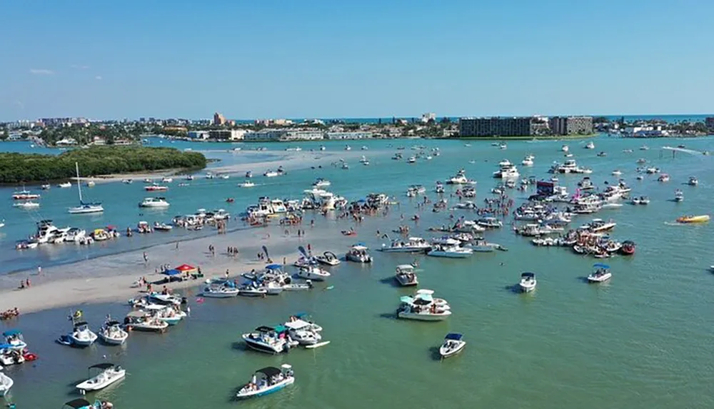 An aerial view of a lively boat gathering with numerous vessels and people congregated in a shallow water area near the coast