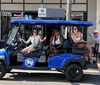 Four individuals are posing with smiles in a blue open-air electric vehicle on a sunny street