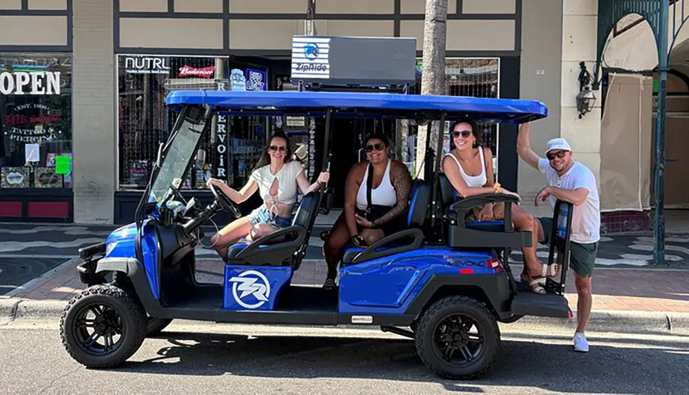 Four individuals are posing with smiles in a blue open-air electric vehicle on a sunny street