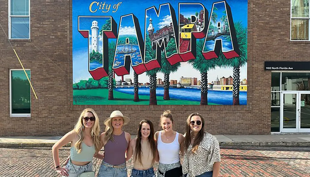 Five individuals are posing for a photo in front of a colorful mural that spells out TAMPA and signifies the city of Tampa Florida