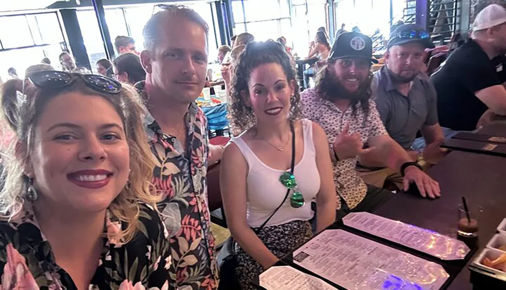 A group of friends are smiling and posing for a photo at a restaurant table with menus in front of them