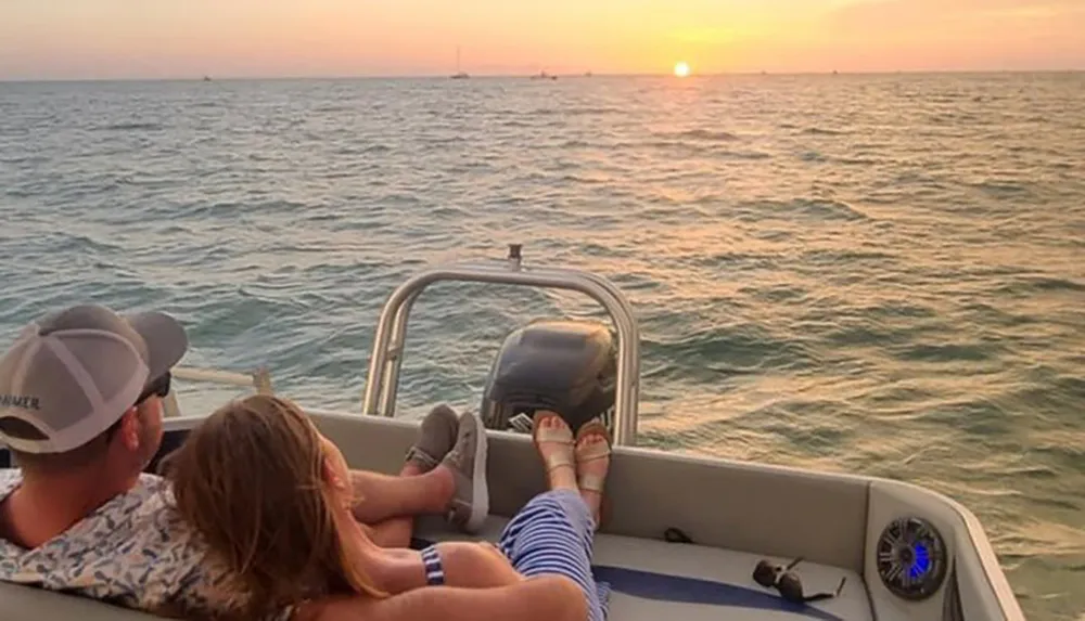 Two people are enjoying a sunset from the back of a boat on the water