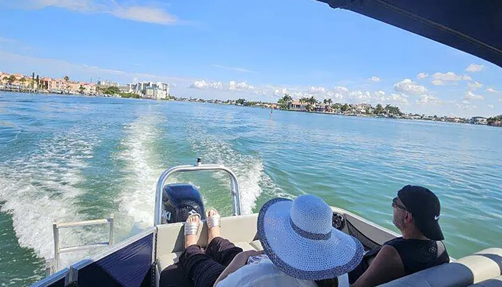 Two individuals are enjoying a boat ride on a sunny day with a view of coastal scenery ahead