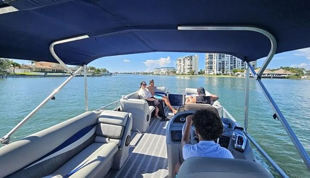 People enjoy a sunny day on a boat cruising through calm waters with buildings in the background