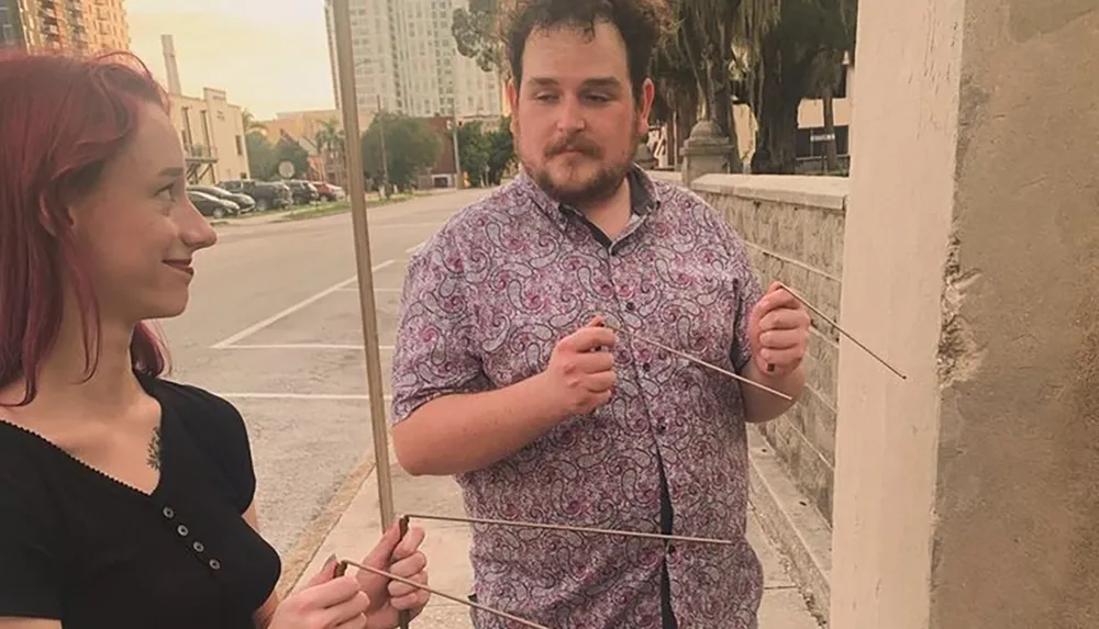 Two people are engaging in what appears to be a playful activity involving sticks on a city street