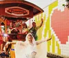 A group of cheerful people some wearing ponchos are enjoying a ride on a pedal pub against a colorful mosaic-tiled wall background