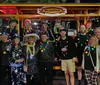 A group of cheerful people some wearing ponchos are enjoying a ride on a pedal pub against a colorful mosaic-tiled wall background