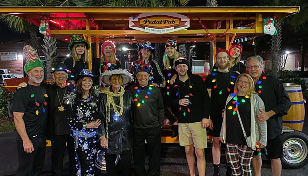 A group of smiling people dressed in festive holiday attire is gathered in front of a Pedal Pub decorated with lights and ornaments for a night out